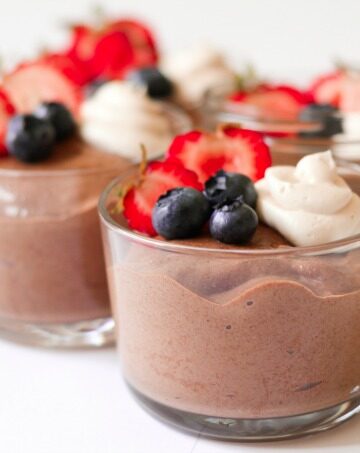 Jars of smooth chocolate chia pudding with berries and cream on the top.