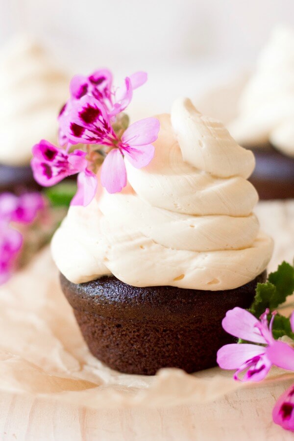 Vanilla buttercream frosting swirled on top of chocolate cupcakes with pink flowers.
