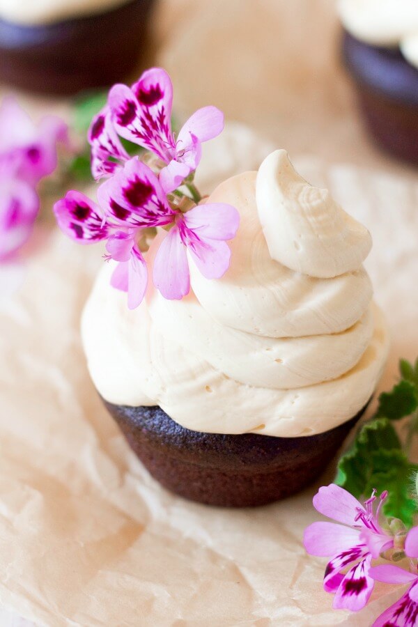 Vanilla buttercream frosting on top of chocolate cupcake with pink flowers.