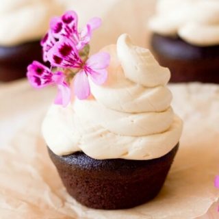 Vanilla buttercream frosting on top of chocolate cupcakes with pink flowers.