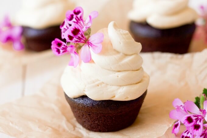 Vanilla buttercream frosting on top of chocolate cupcakes with pink flowers.