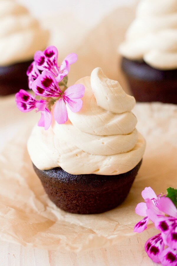 Vanilla buttercream frosting on top of chocolate cupcakes with pink flowers.