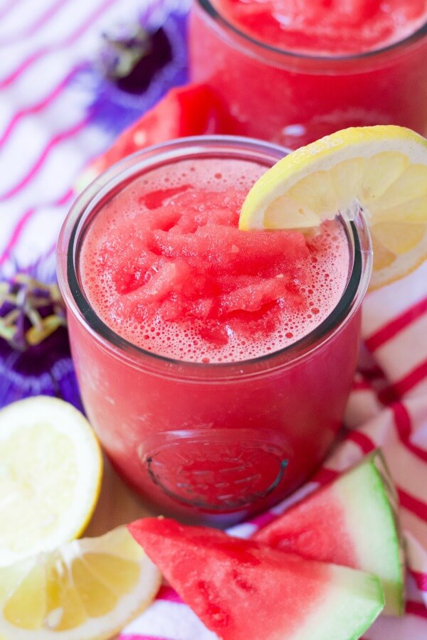 Glasses filled with pink watermelon lemonade slushy with fresh lemon slices and watermelon pieces.