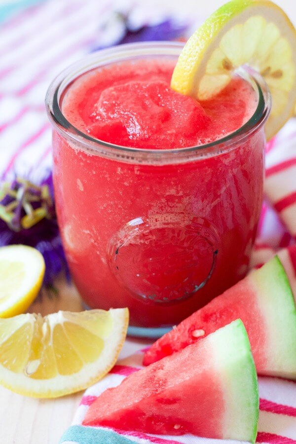 Glass full of pink slushy watermelon lemonade with fresh lemon slices and watermelon slices.