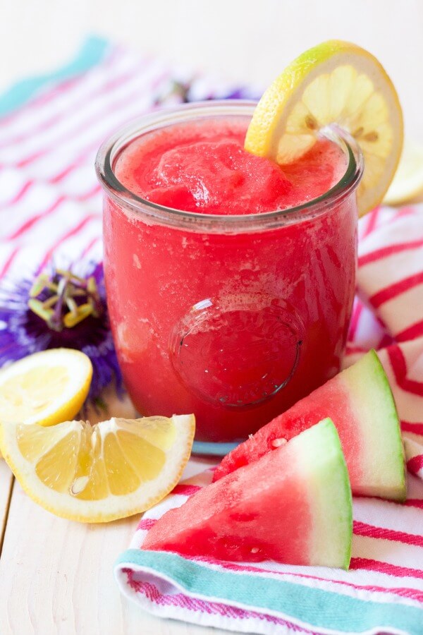 Glass of pink slushy watermelon lemonade with fresh lemon slices and watermelon slices.