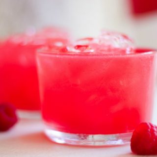 Glasses with pink raspberry soda and fresh raspberries.