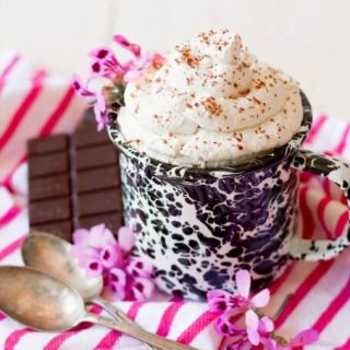 Mug full of whipped cream with chocolate shaved over the top and chocolate on the side.