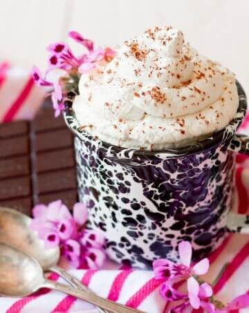 Mug full of whipped cream with chocolate shaved over the top and chocolate on the side.