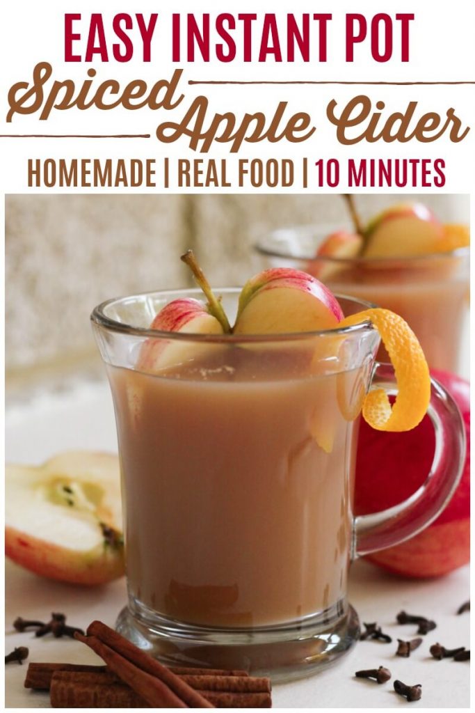 Glass mug full of apple cider, sliced apples and orange zest.