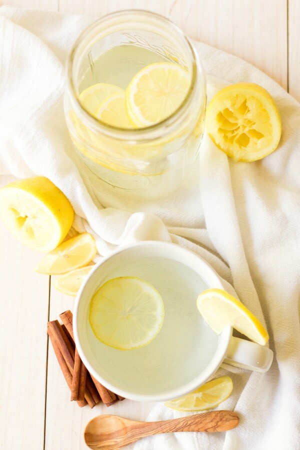 Mason jar and mug with hot drink and lemon slices with cinnamon sticks.