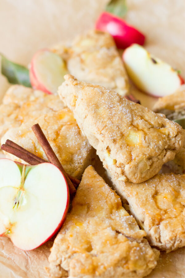 Stack of apple scones with fresh apples and cinnamon sticks.