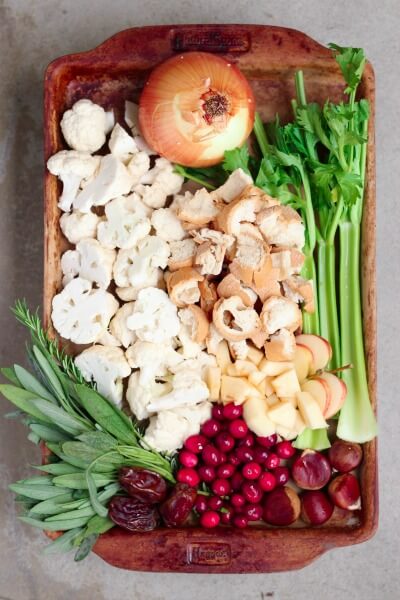 Baking sheet with celery, bread cubes, cauliflower, onion, cranberries, fresh herbs, dates and chestnuts.