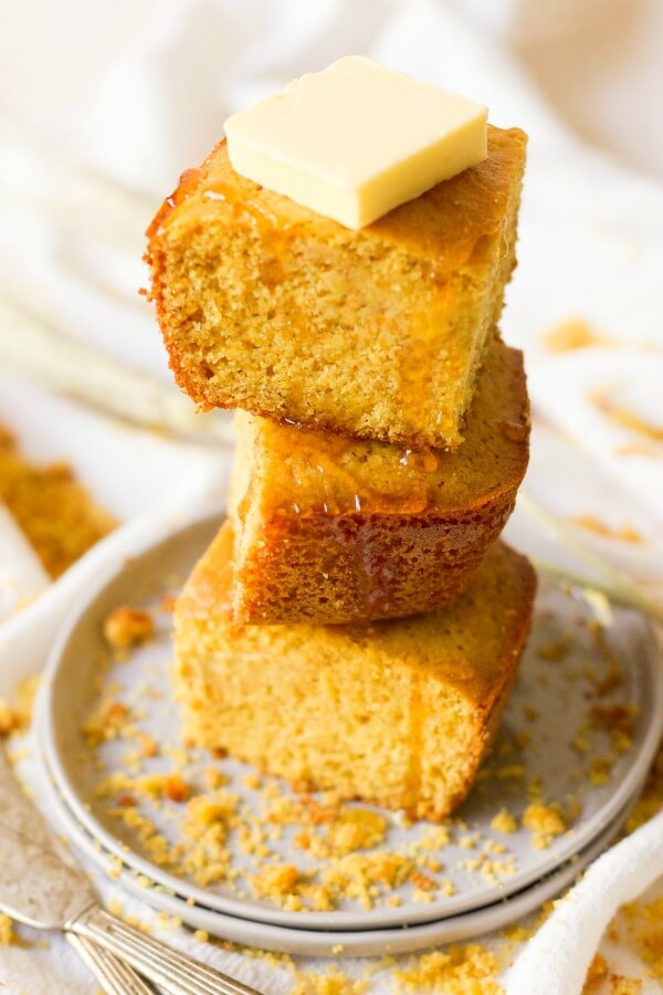 Stack of cornbread slices with butter and honey drizzle.