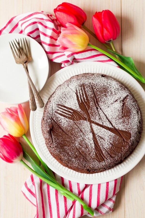 Chocolate torte cake dusted with powdered sugar making two forks pattern next to tulips.