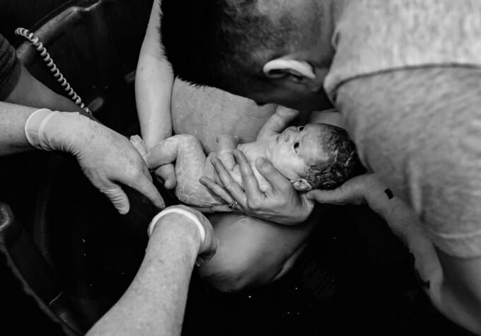 Infant baby just born at home during a water birth home birth into the hands of his mother and father.