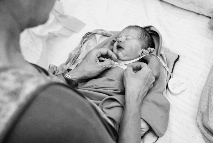 Newborn baby being measured during his newborn exam at home by his midwife after his home birth.