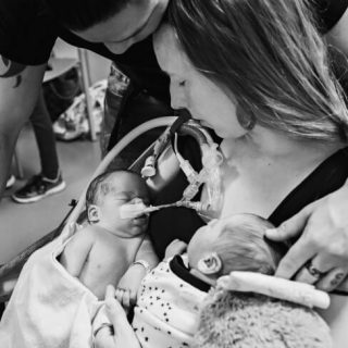 Grieving mother and father of twins with the mother holding both infant babies, one who is sleeping and one who is on life support in the NICU.