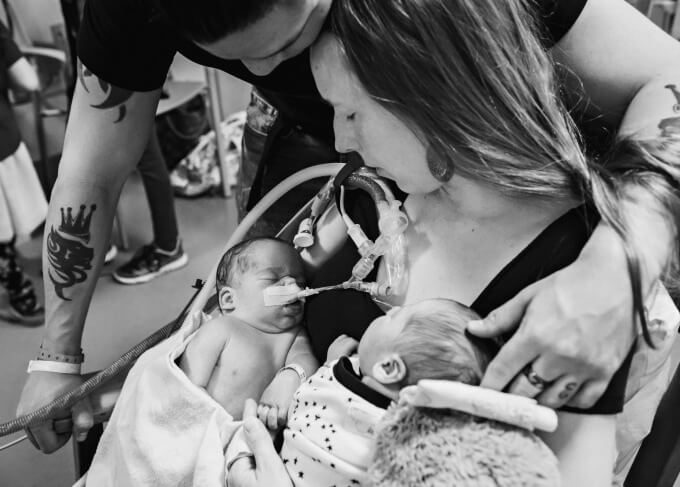 Grieving mother and father of twins with the mother holding both infant babies, one who is sleeping and one who is on life support in the NICU.