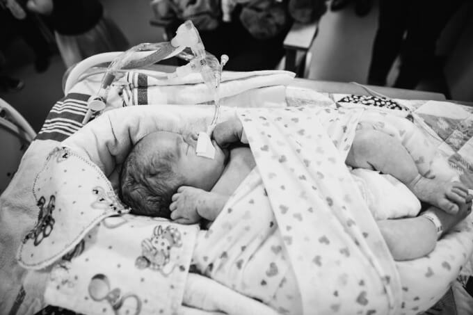 Newborn baby wrapped up in his bed in the NICU surrounded by family.