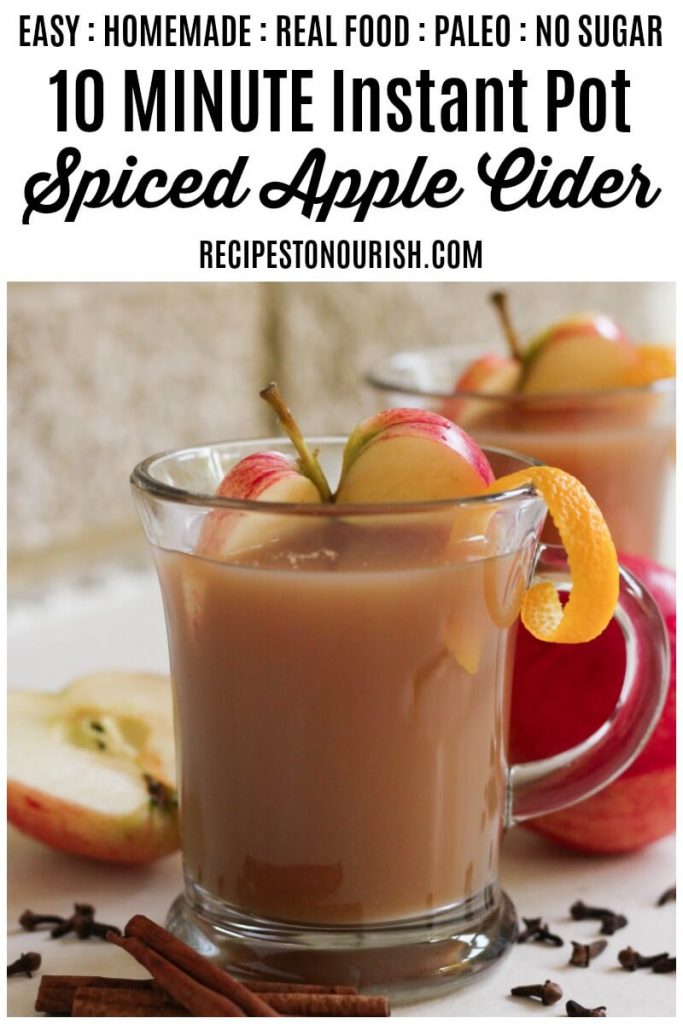 Glass mugs filled with spiced apple cider, fresh apple slices, orange peel, cinnamon and cloves.