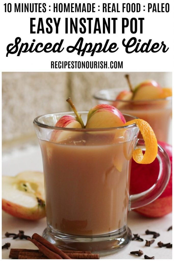 Glass mugs filled with spiced apple cider, fresh apple slices, orange peel, cinnamon and cloves.