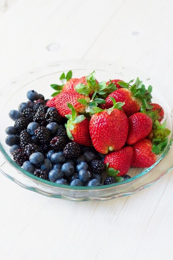 Glass dish full of fresh strawberries, blueberries and blackberries.
