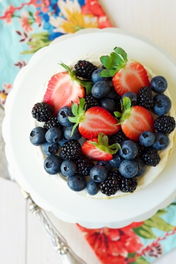 Overhead view of a cheesecake tart topped with fresh blueberries, strawberries and blackberries sitting on a cake stand.