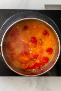 Overhead view of saucepan cooking homemade tomato sauce with fresh cherry tomatoes.