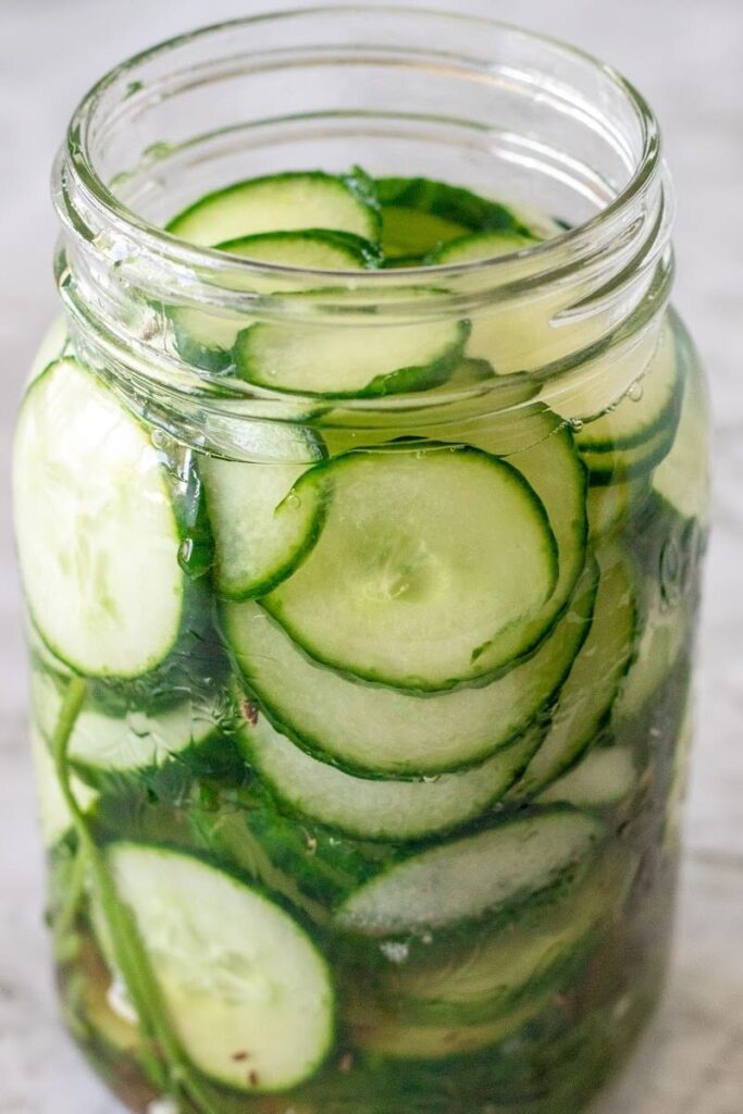 Side profile of mason jar filled with sliced pickles and fresh dill sprigs.