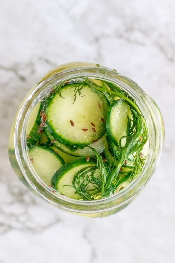 Overhead shot of a mason jar filled with sliced pickles, fresh dill, spices and liquid brine.