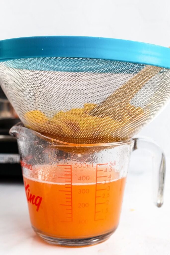 A glass measuring cup filled with peach liquid and a large fine mesh strainer sitting on top of it with cooked peach pulp.