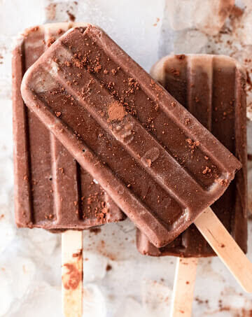 Several fudgesicle popsicles dusted with cocoa powder sitting on top of ice.