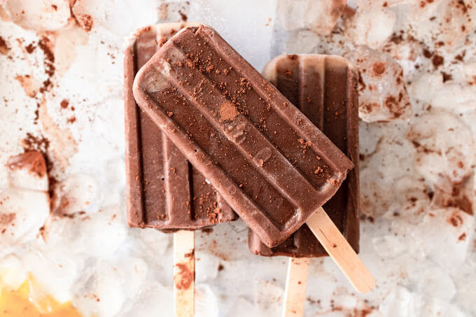 Several fudgesicle popsicles dusted with cocoa powder sitting on top of ice.