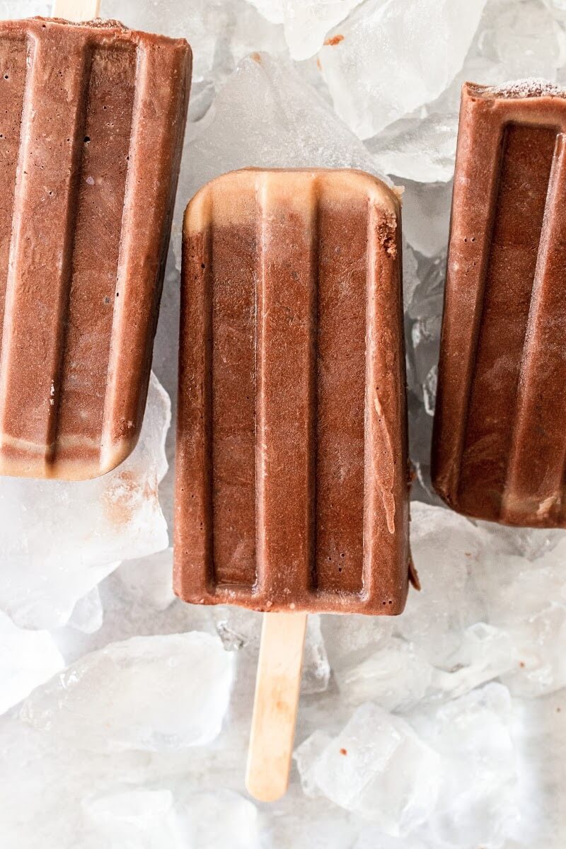 3 fudgesicle popsicles sitting on top of ice.