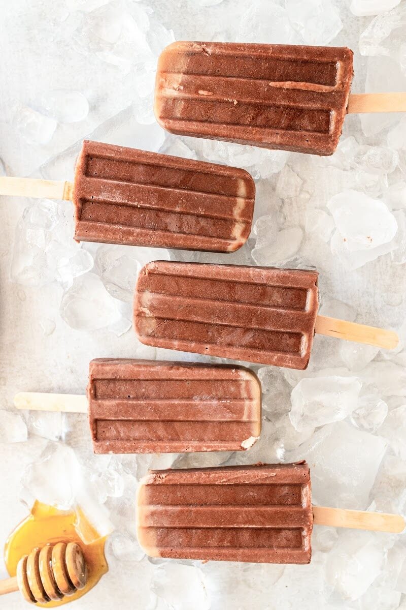 5 fudgesicle popsicles sitting on top of ice, next to a honey dipper with honey on it.