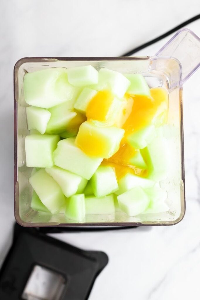 An open blender filled with chunks of honeydew melon and honey.