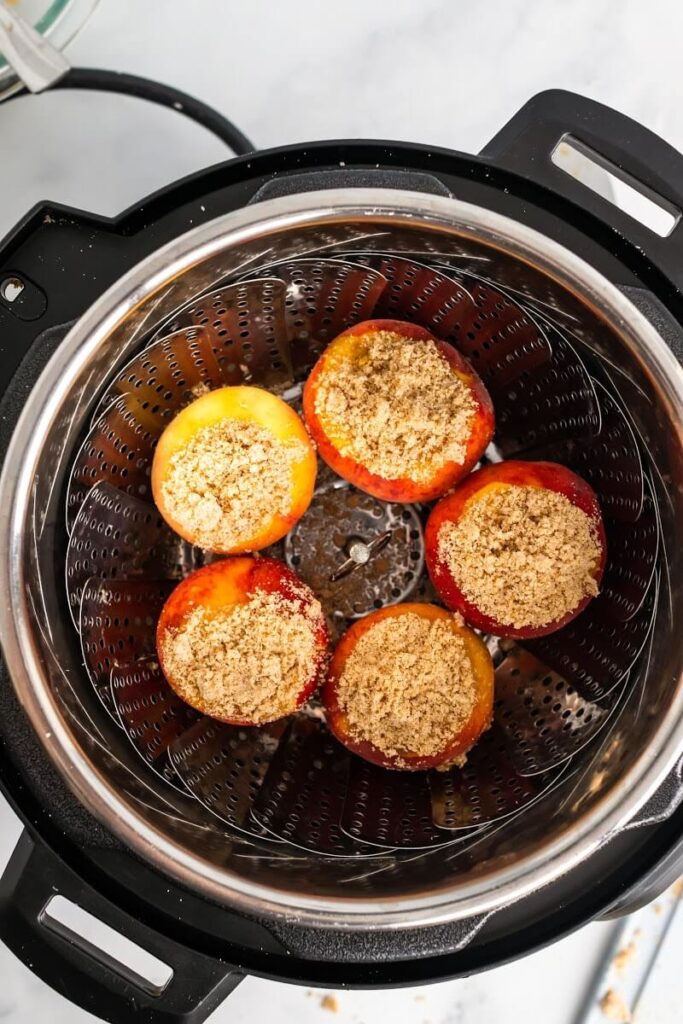 A steamer basket insert inside an Instant Pot with 5 uncooked stuffed peaches sitting in the steamer basket insert.