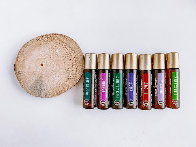 A round wooden slice of a tree next to 7 roll-on Young Living essential oil bottles.