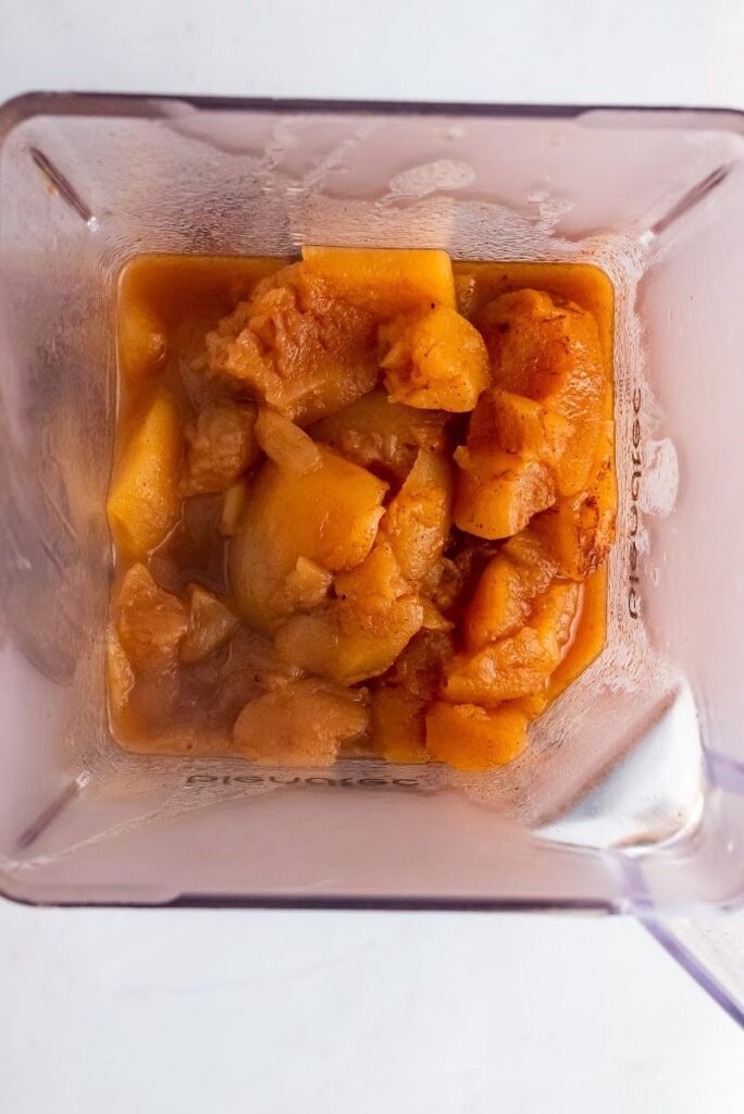 Overhead view of a blender filled with hot, cooked and quartered, cinnamon apples.