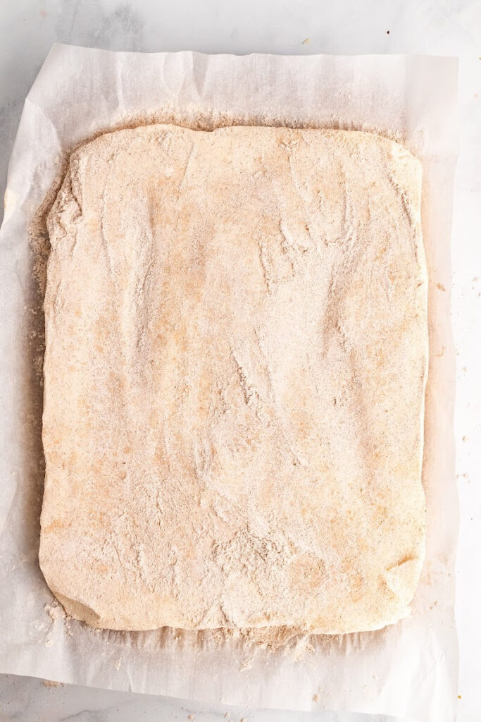 Parchment paper sitting on top of a counter with uncut homemade marshmallows that are fully covered and dusted with an arrowroot-ground cinnamon mixture on top.