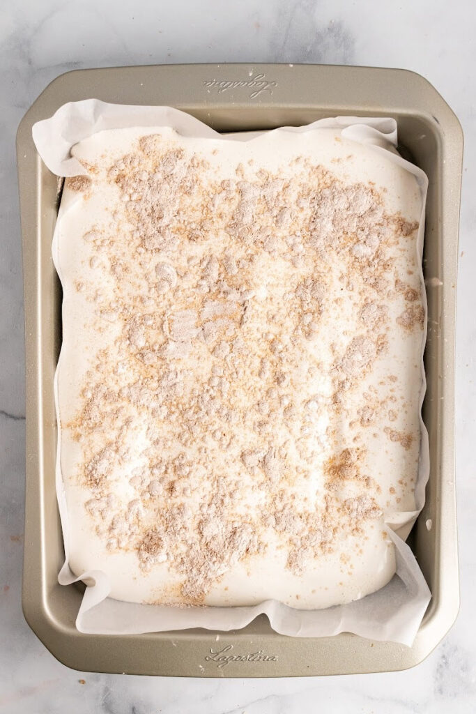 A rectangle baking pan lined with parchment paper and filled with uncut homemade marshmallows that are sprinkled with an arrowroot-ground cinnamon mixture on top.