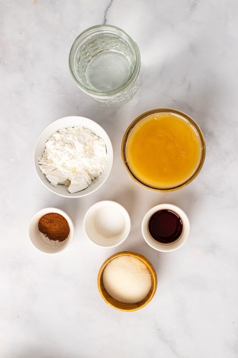 Photo of recipe ingredients with a jar full of water, a bowl full of honey, a bowl full off arrowroot powder, a small bowl full of ground cinnamon, a small bowl full of vanilla extract, a small bowl of gelatin and a small bowl of salt.