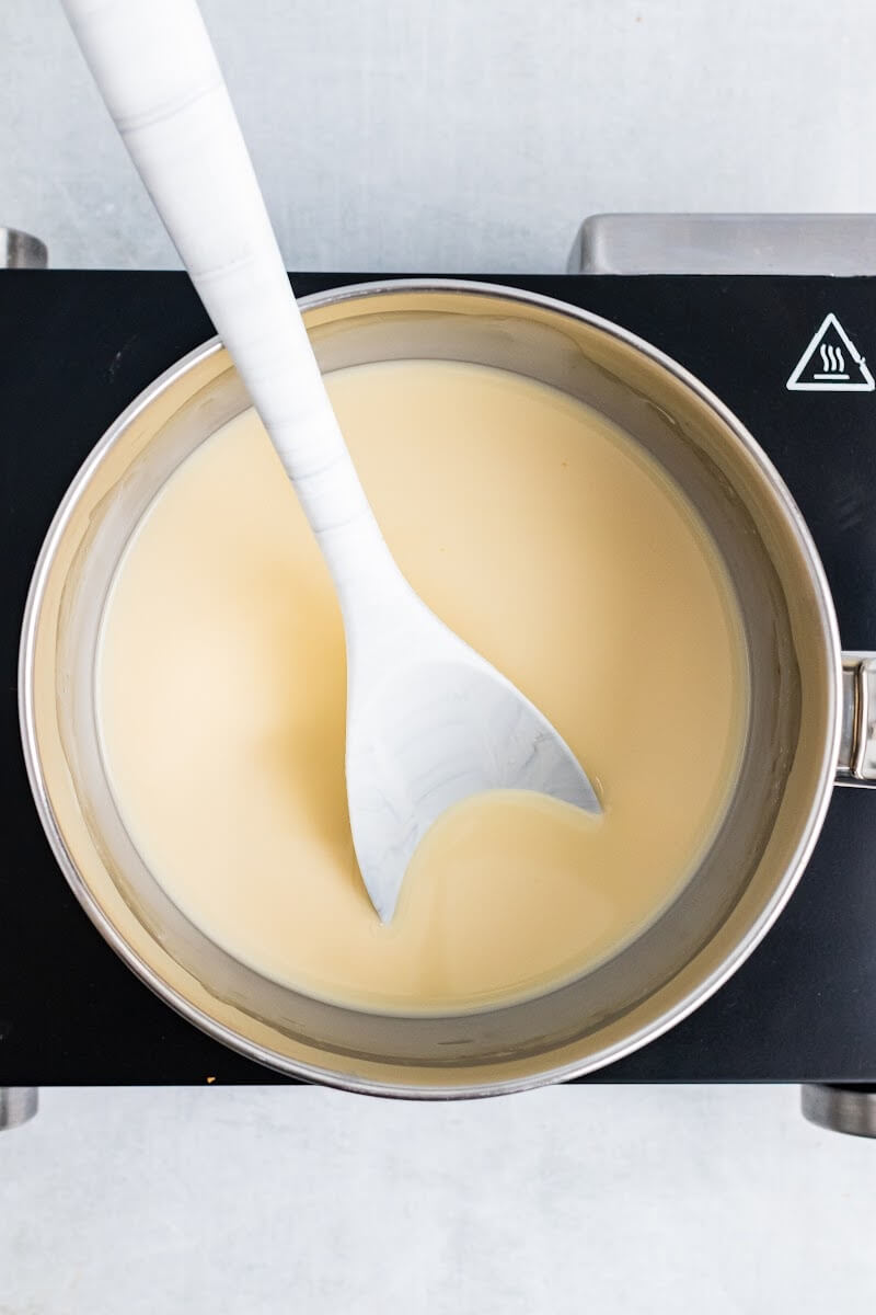 Saucepan with cream and vanilla extract mixture with a spoon stirring.