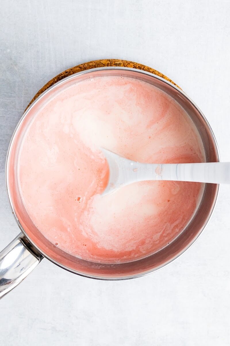 Saucepan with creamy watermelon mixture and a spoon stirring.