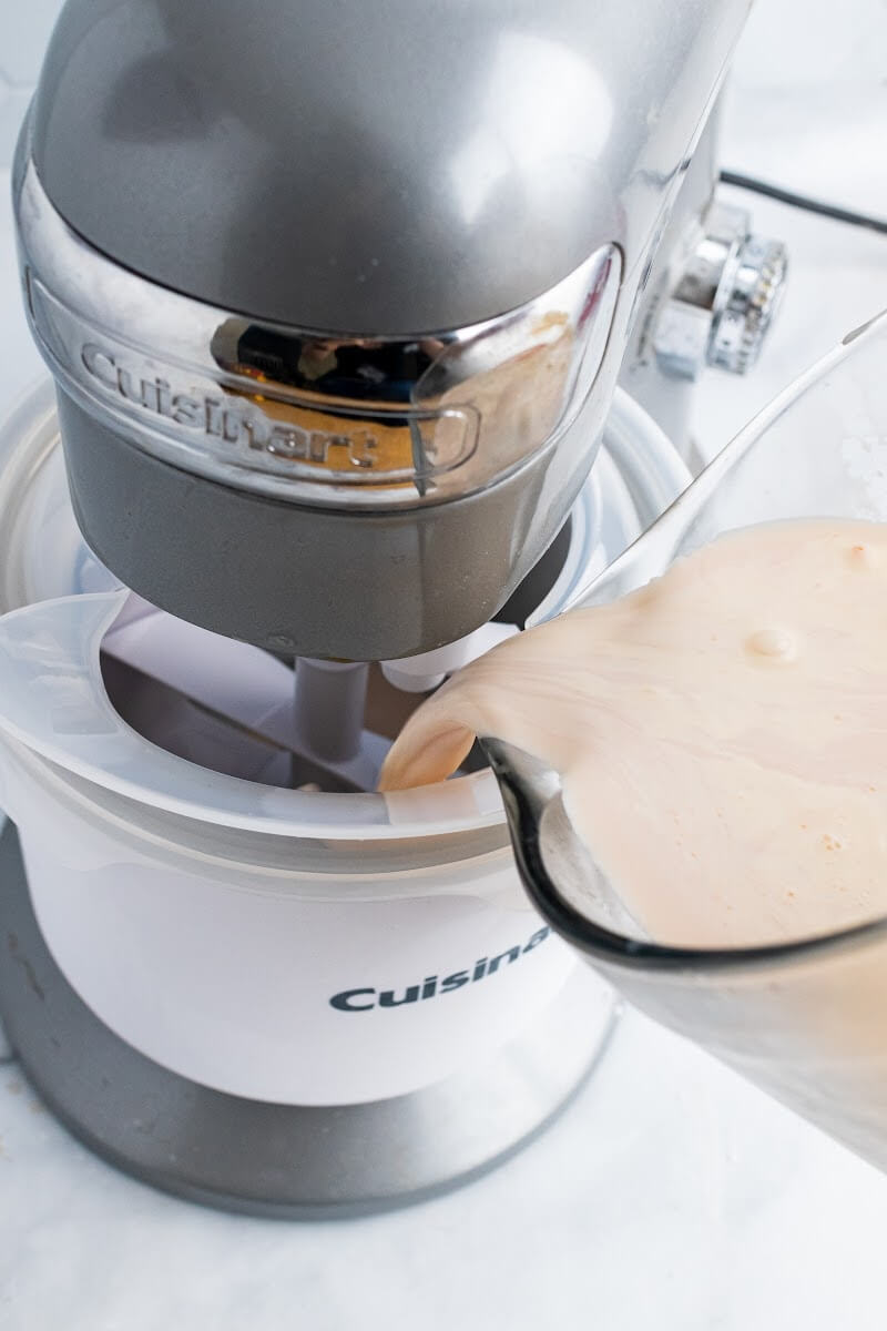 Glass measuring cup pouring ice cream mixture into a Cuisinart ice cream maker.