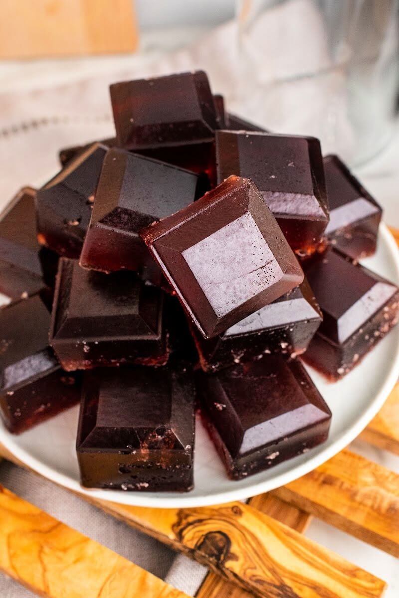 Plate with stacks of dark purple homemade gelatin gummies, sitting on top of a wooden board.