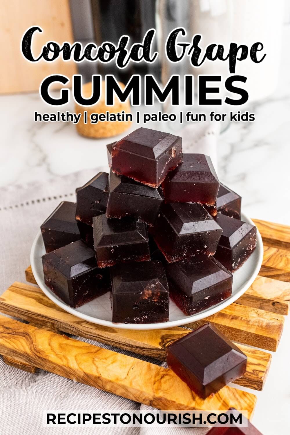 Plate with stacks of dark purple homemade gelatin gummies, sitting on top of a wooden board and text that says Concord grape Gummies, healthy, gelatin, paleo, fun for kids.
