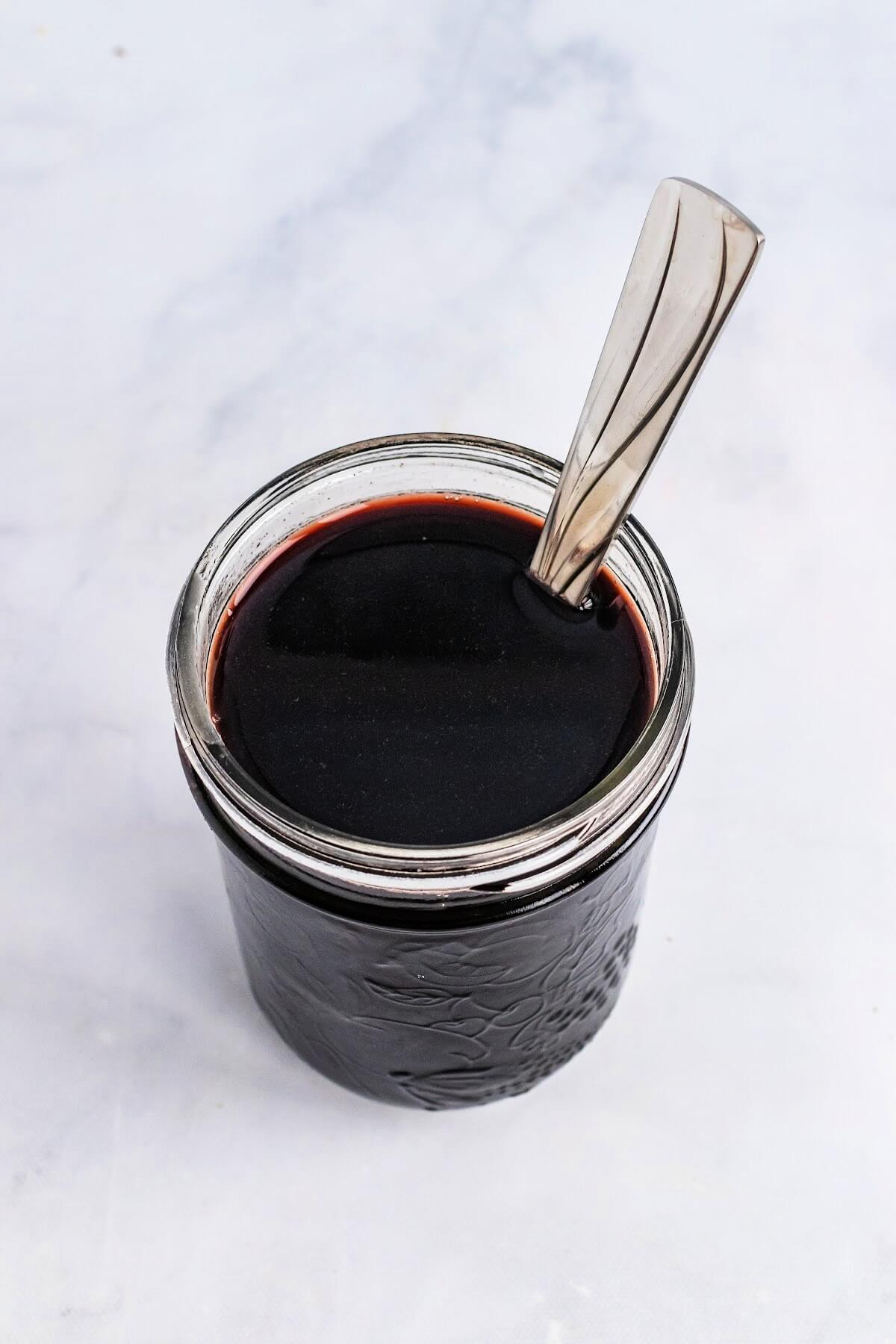 Overhead view of a mason jar filled with a dark purple syrup with a spoon sitting inside of the jar.