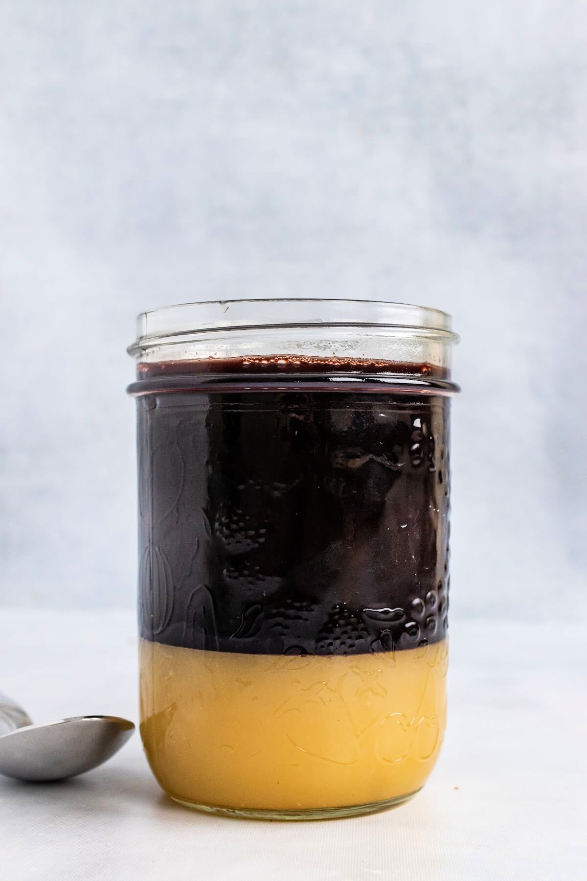 Mason jar ¾ filled with a dark purple syrup and ¼ filled at the bottom with honey, with a spoon sitting next to it.