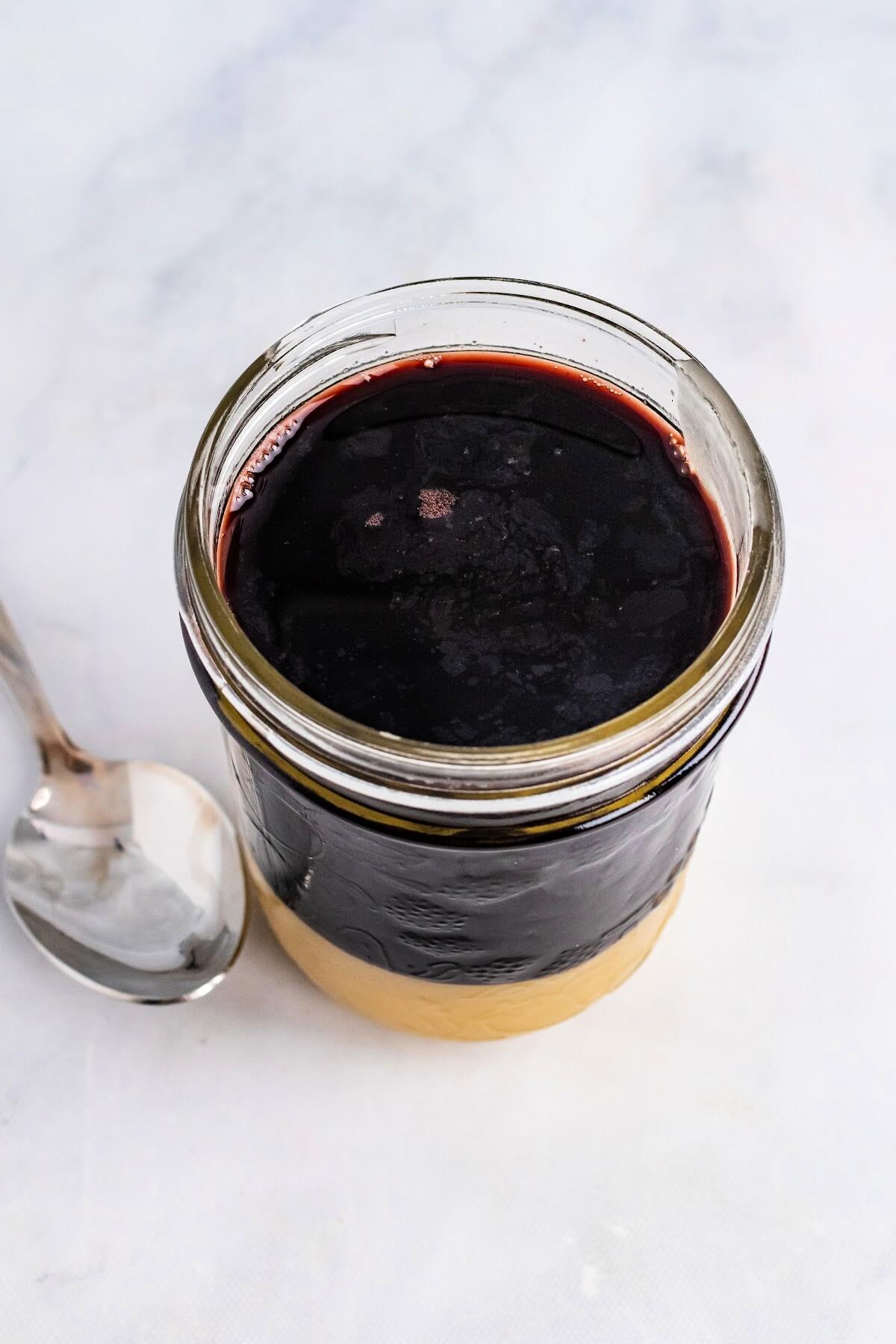 Overhead view of a mason jar ¾ filled with a dark purple syrup and ¼ filled at the bottom with honey, with a spoon sitting next to it.